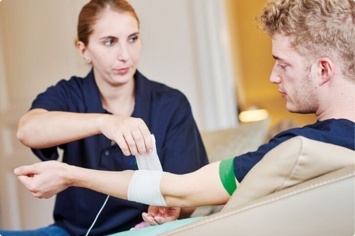 Spazialisierte Fachperson legt einen venösen Zugang bei einem jungen Erwachsenen.